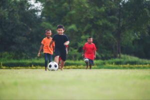 Kids playing soccer outdoors , staying active, learning teamwork, and building strength while reducing sports injury risk.