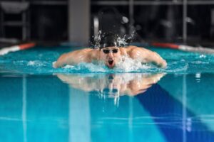Competitive swimmer performing butterfly stroke in an indoor pool, showcasing upper body strength, shoulder mobility, and precise breathing technique, representing efficient biomechanics in swimming