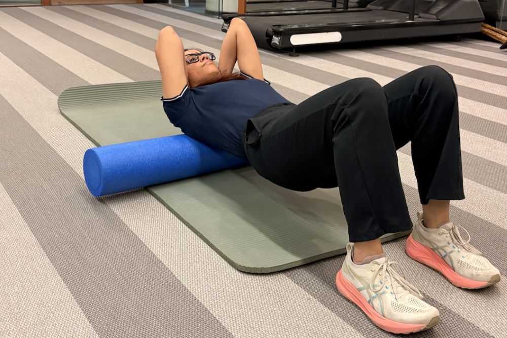 Person performing foam roller exercise for back mobility and recovery in a physiotherapy gym setup - VARDĀN
