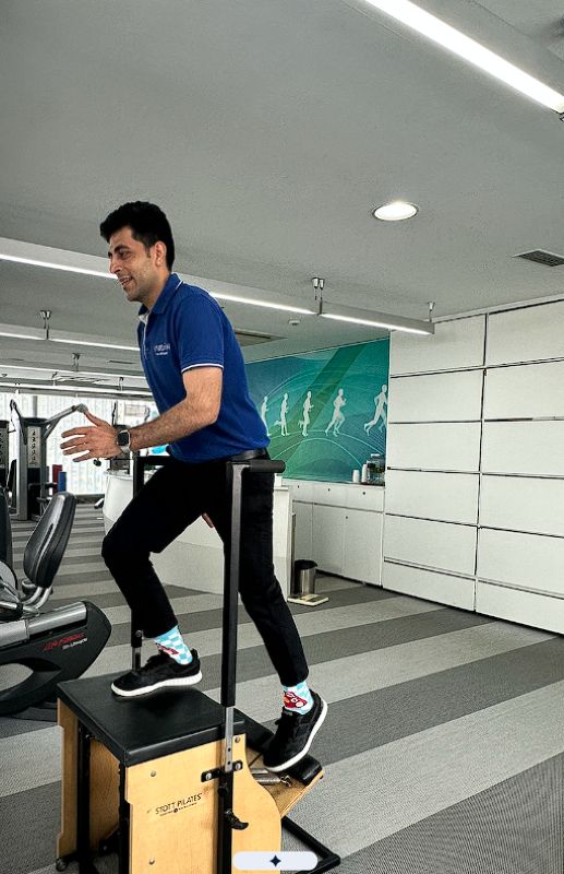 VARDĀN trainer demonstrating step-up exercise on Pilates chair machine for strength and rehabilitation training